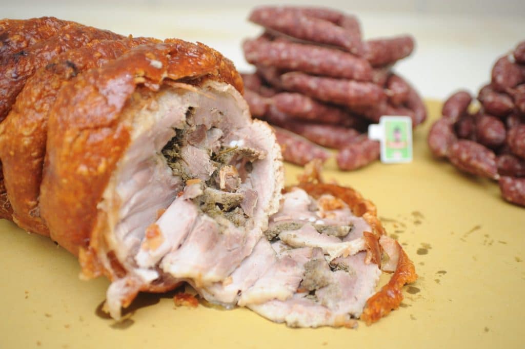 Porchetta affettata con salsicce sullo sfondo.