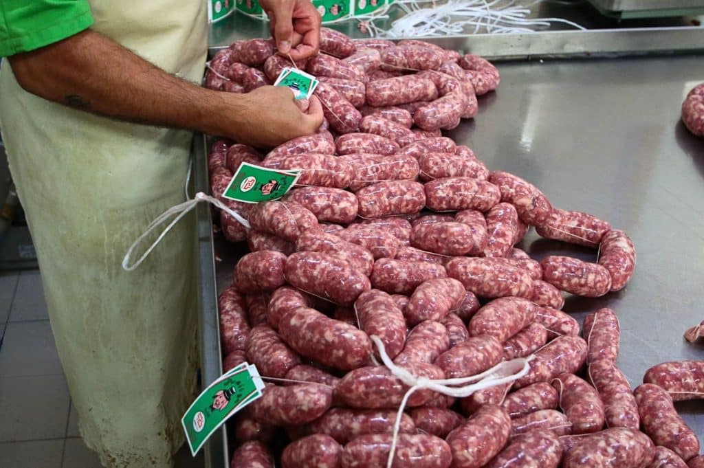 Persona etichetta salsicce su tavolo metallico.
